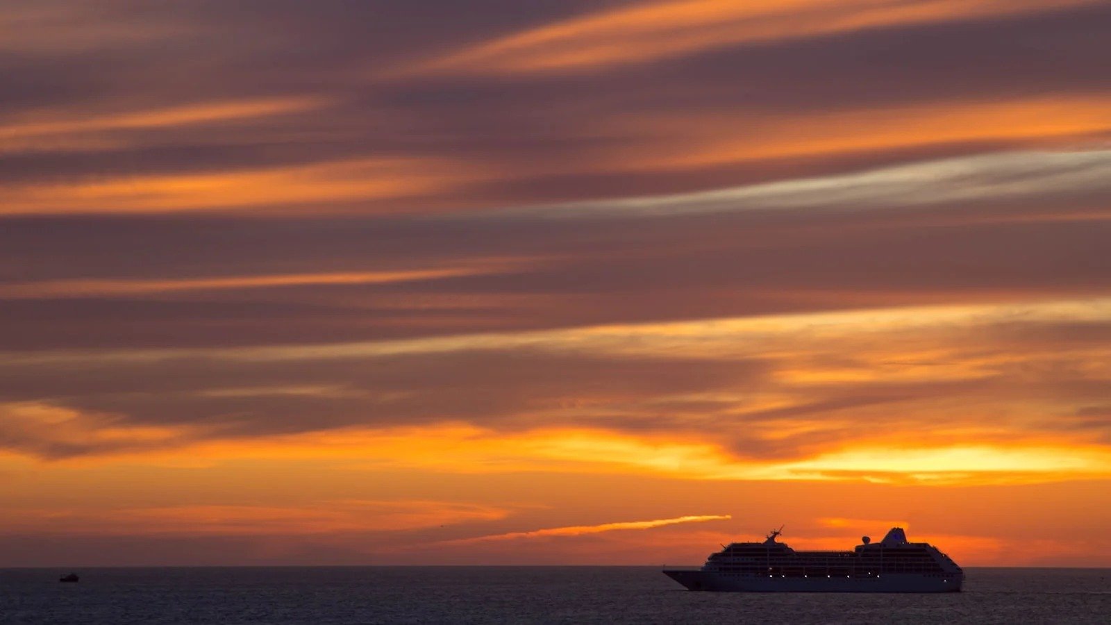 Cruise ship sailing away under an orange sunset sky